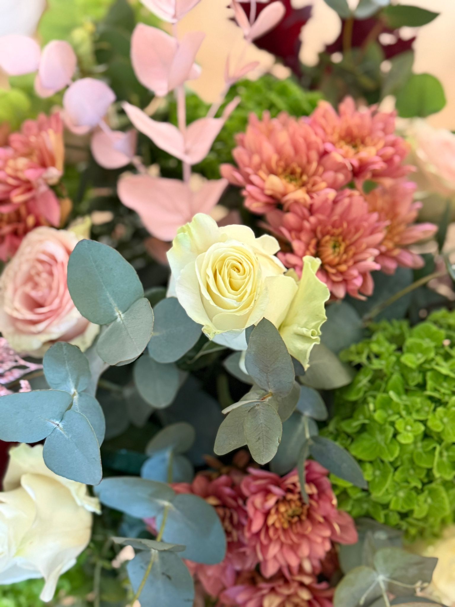 Ramo de flores secas de colores en un jarrón con lentejuelas rojas y cintas, sobre una superficie de madera.