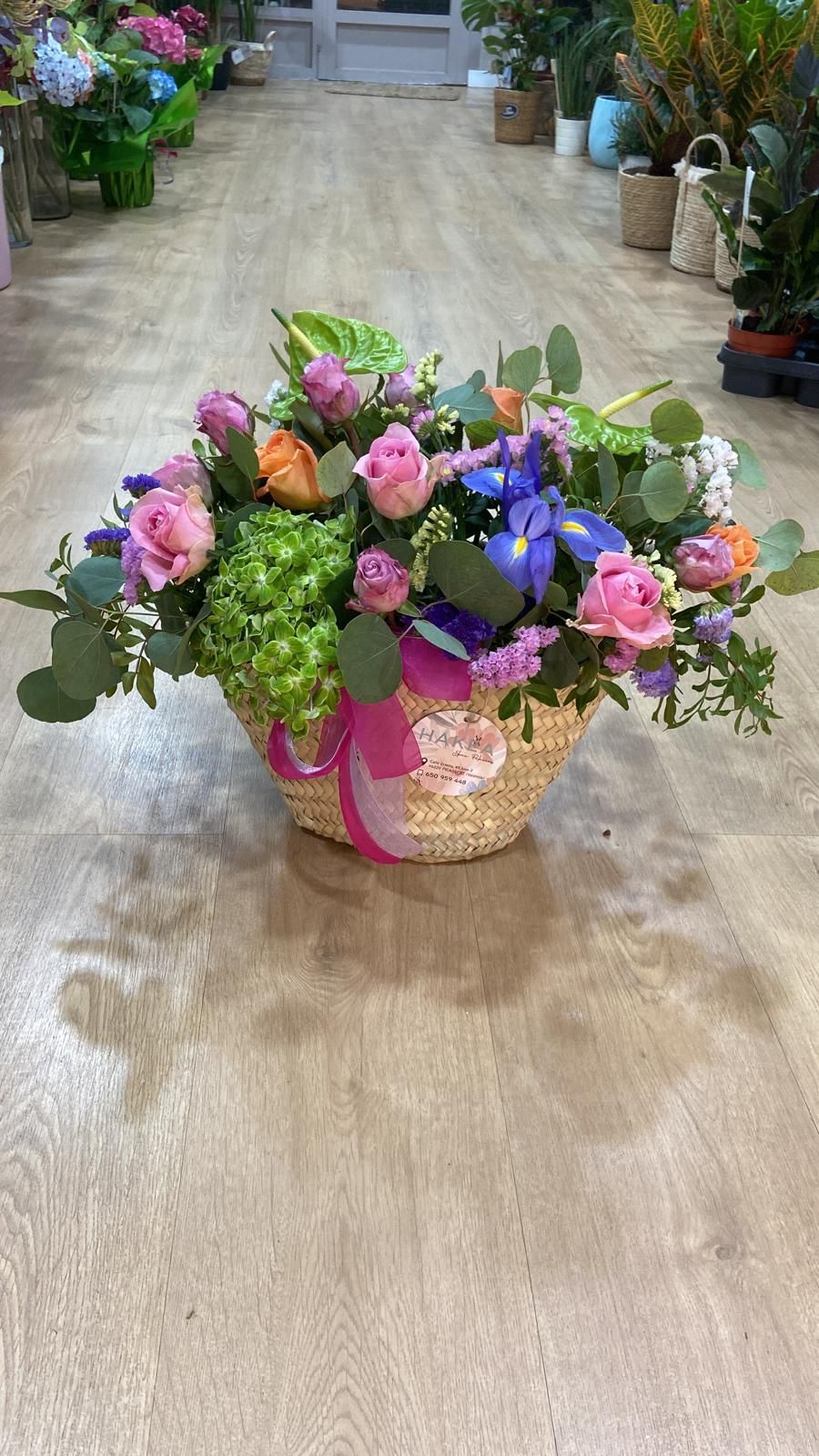 Cesta de flores de colores con rosas rosadas y lirios azules sobre un suelo de madera.