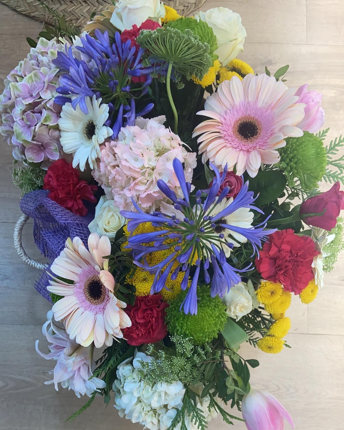 Arreglo floral colorido con margaritas gerberas rosas, agapantos azules y hortensias.