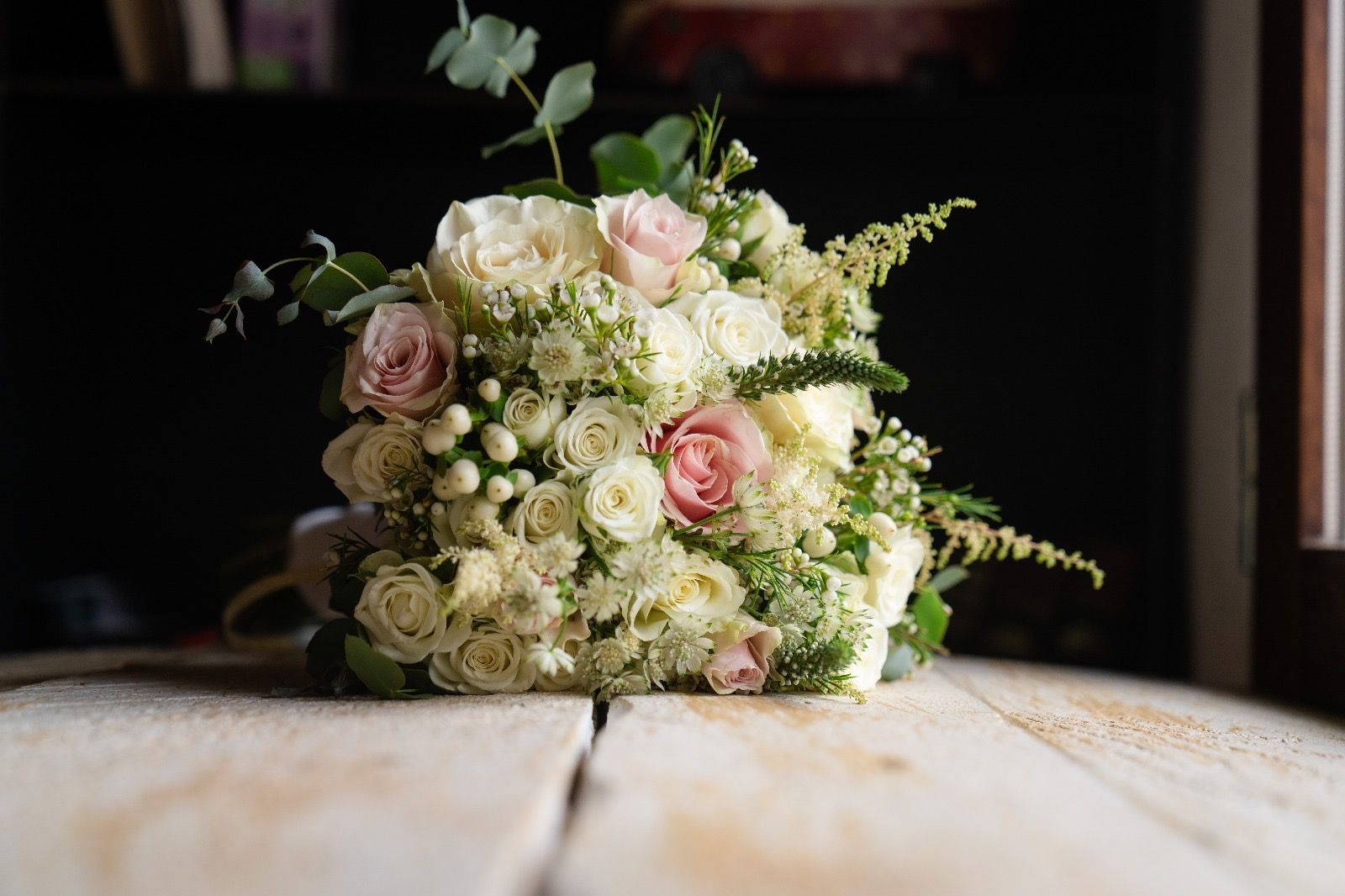 Ramo de rosas blancas y rosadas, vegetación sobre una superficie de madera rústica.