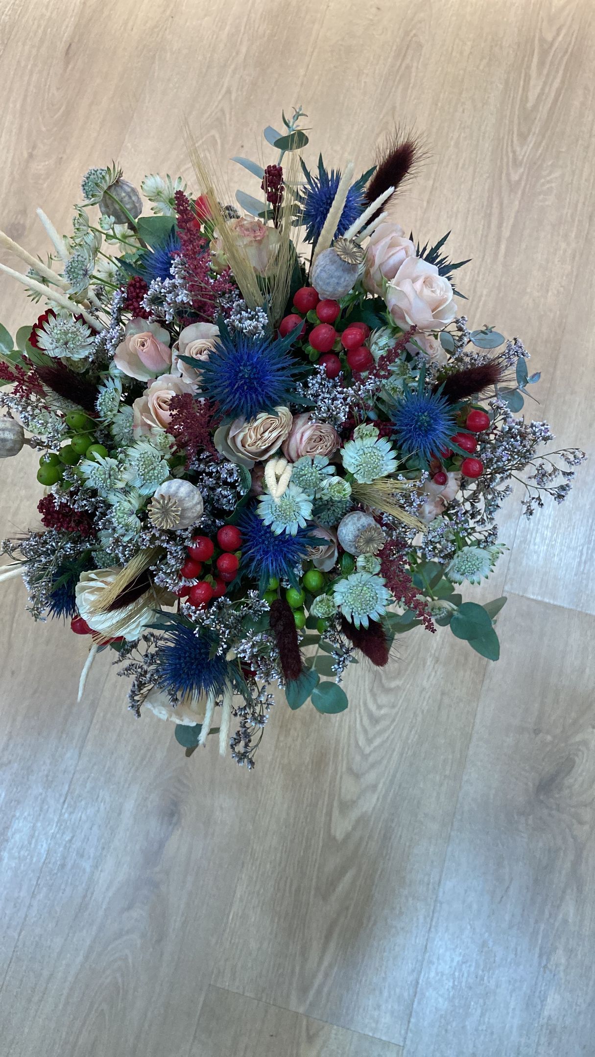 Ramo de flores con flores azules, rojas y blancas y vegetación sobre un fondo de madera clara.