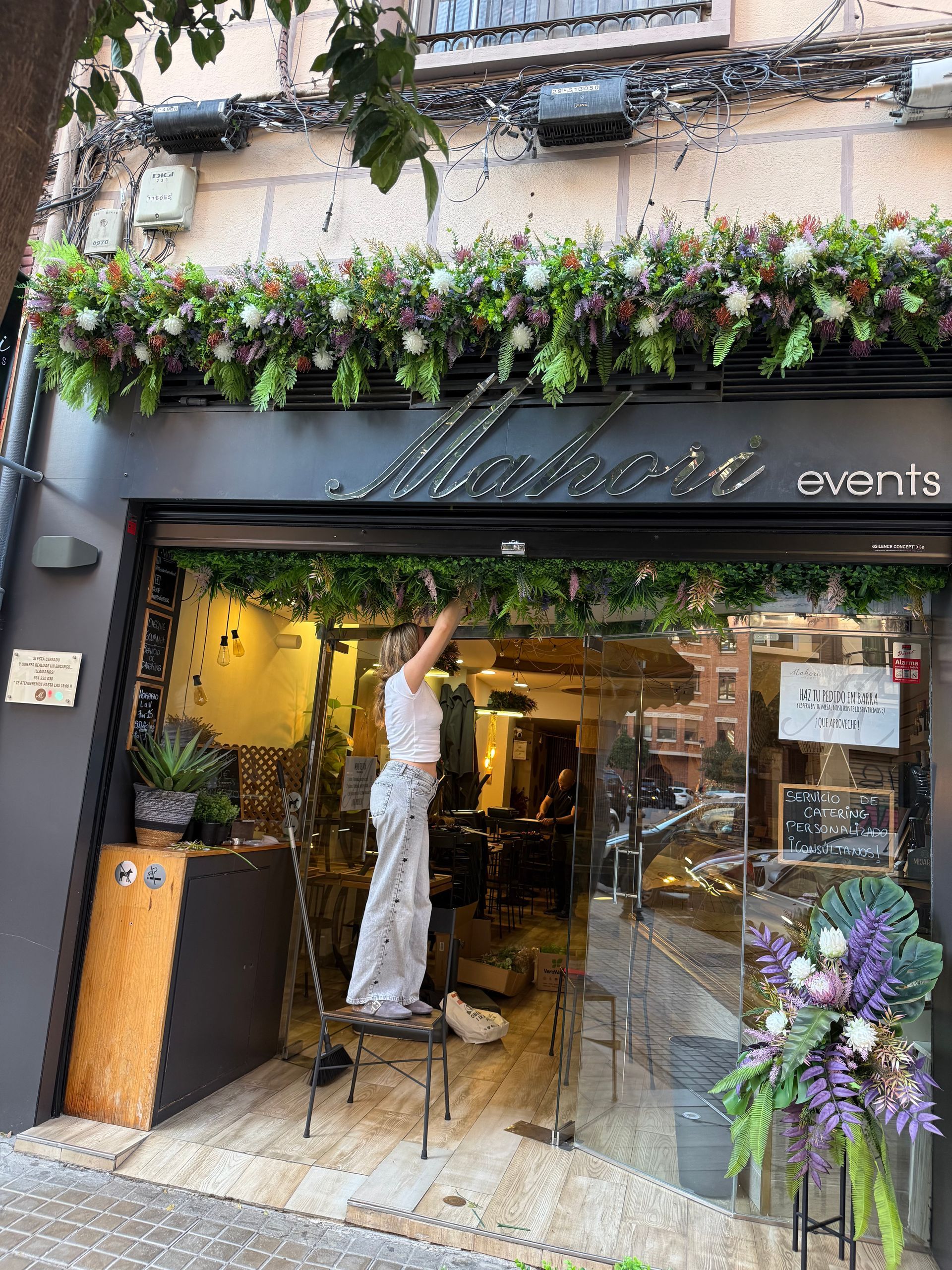 Mujer arreglando un arreglo floral encima de una tienda con un cartel que dice 