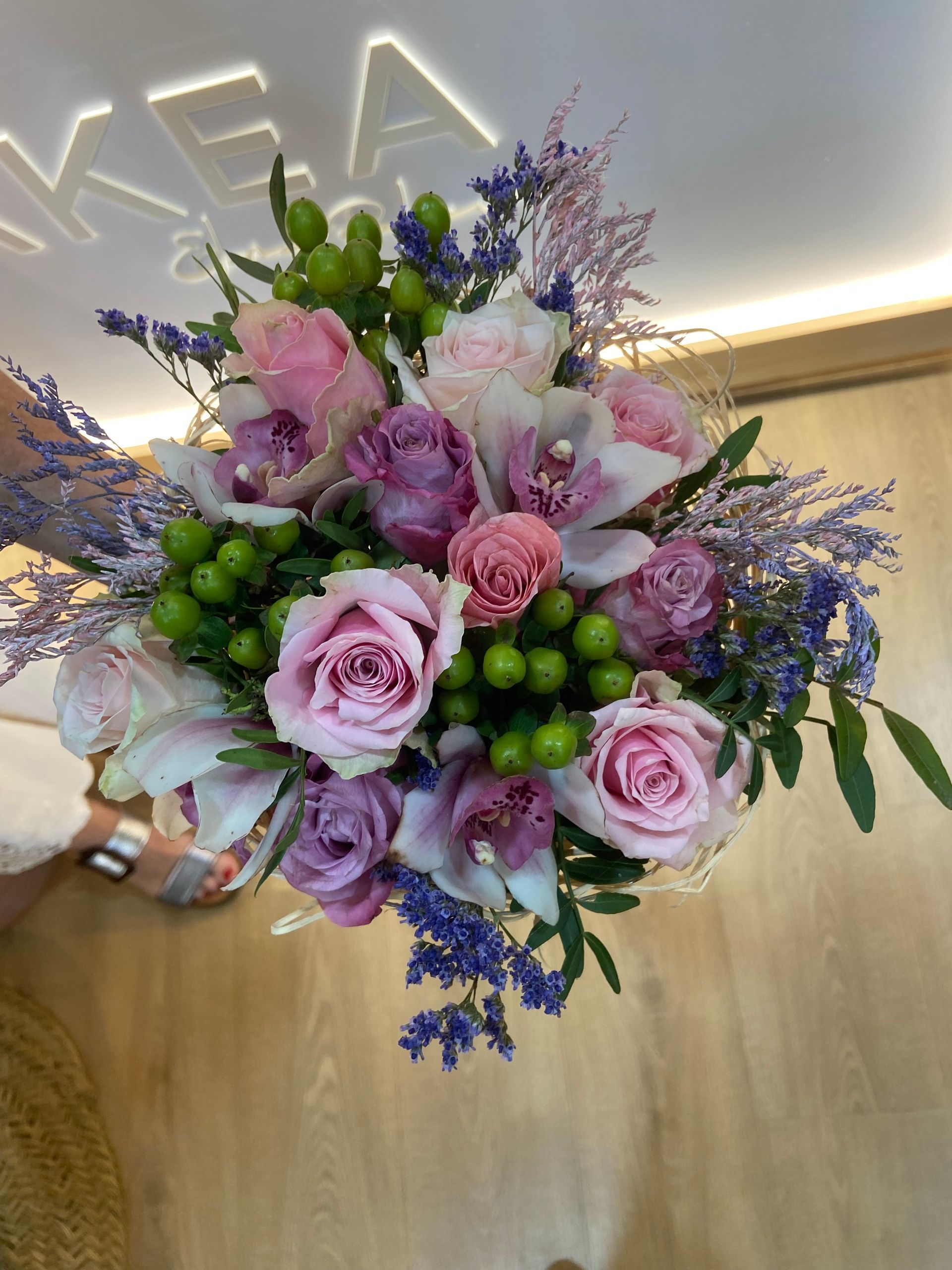 Ramo de rosas rosas y moradas, bayas verdes y ramitas moradas; sostenido sobre un fondo de madera.