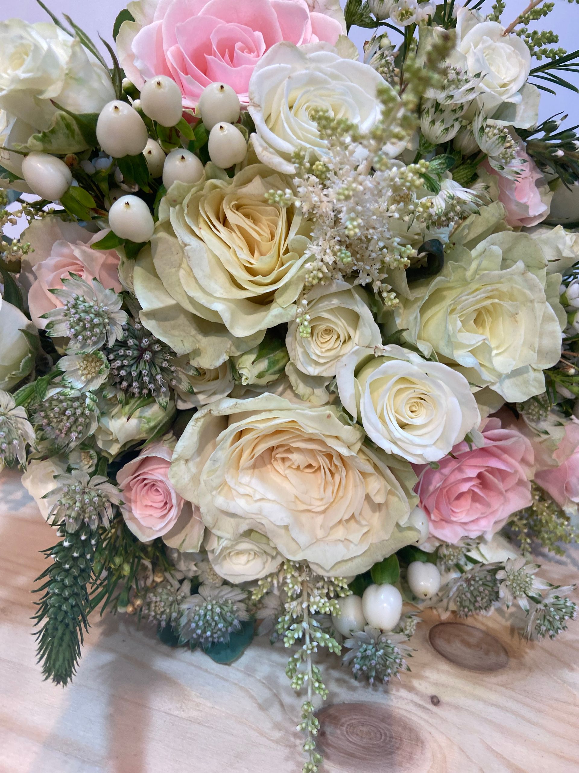 Primer plano de un ramo con rosas de color rosa claro y blanco, rosas de col de color verde pálido y bayas blancas.