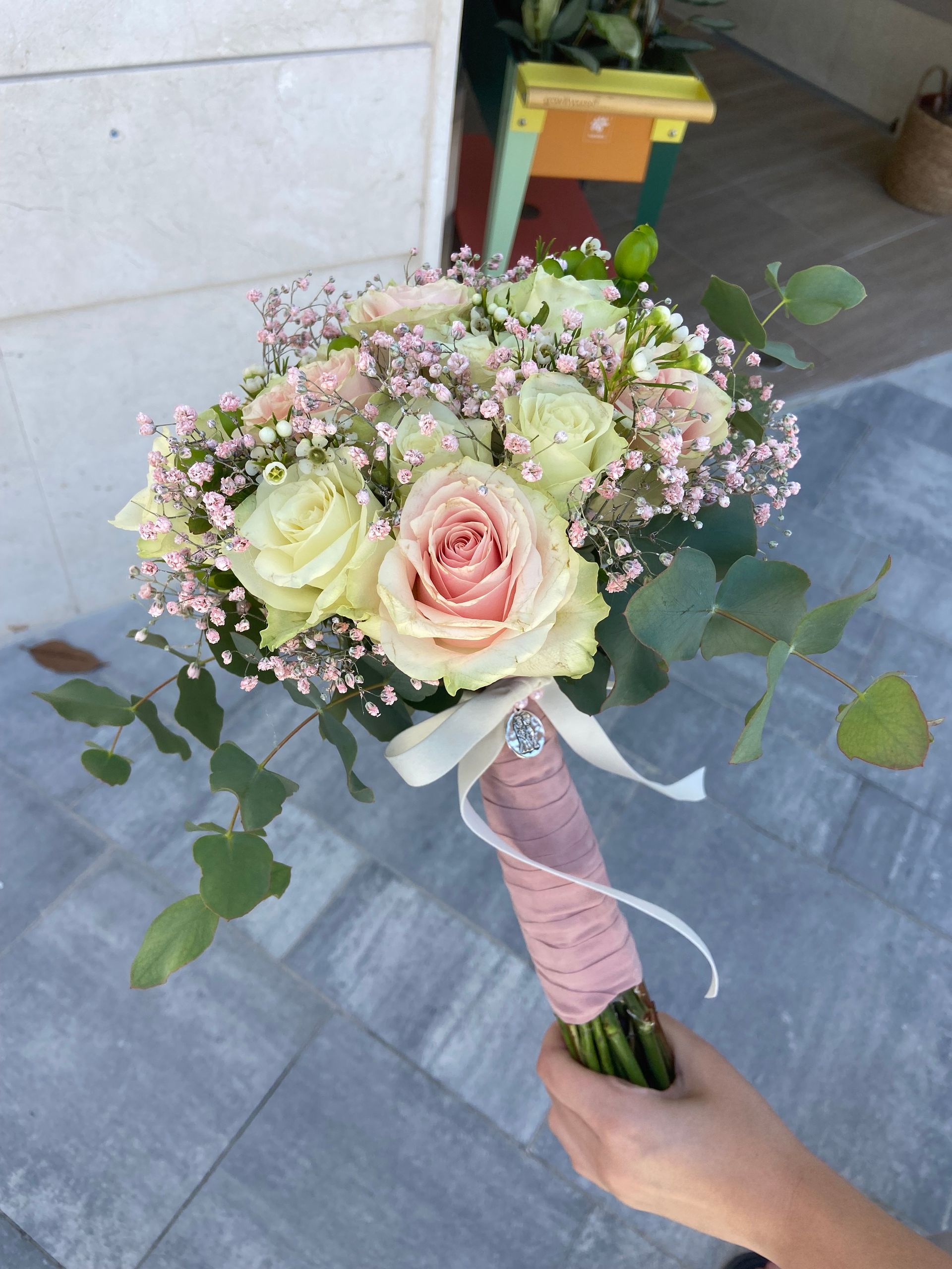 Mano sosteniendo un ramo de novia con rosas rosas y crema, flores de aliento y vegetación; asa envuelta.