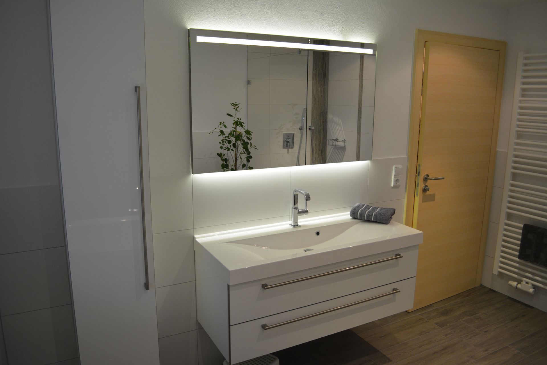 Ein weißes Badezimmer mit weitem Spiegel und integrierter Beleuchtung