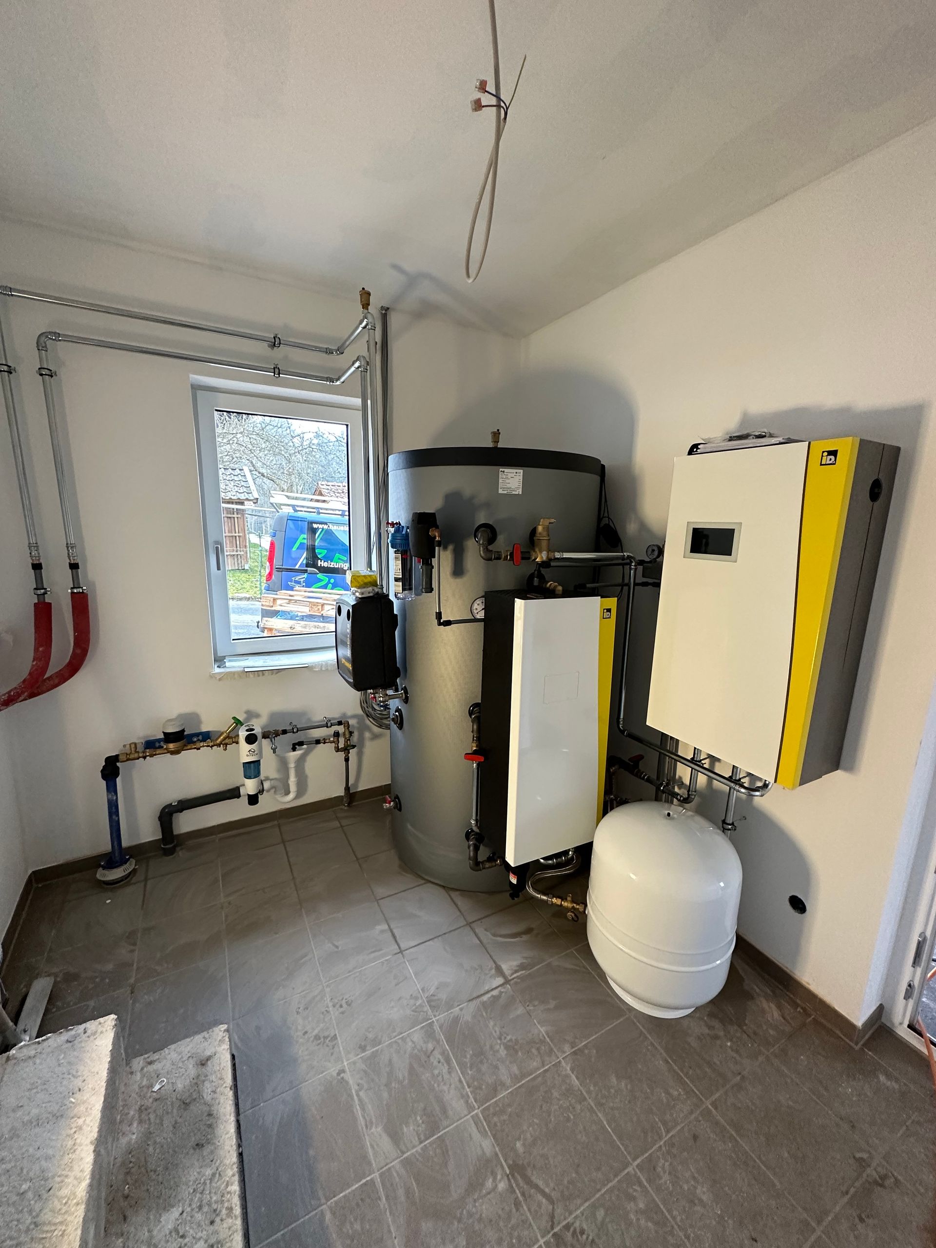 Heizungsraum mit Wandgerät, Warmwasserspeicher und isolierten Rohrleitungen.