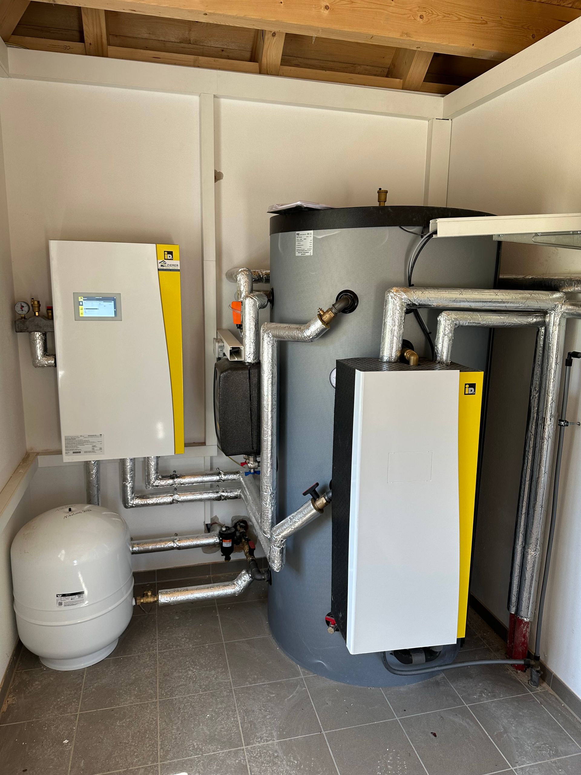 Heizungsraum mit Wandgerät, Warmwasserspeicher und isolierten Rohrleitungen.