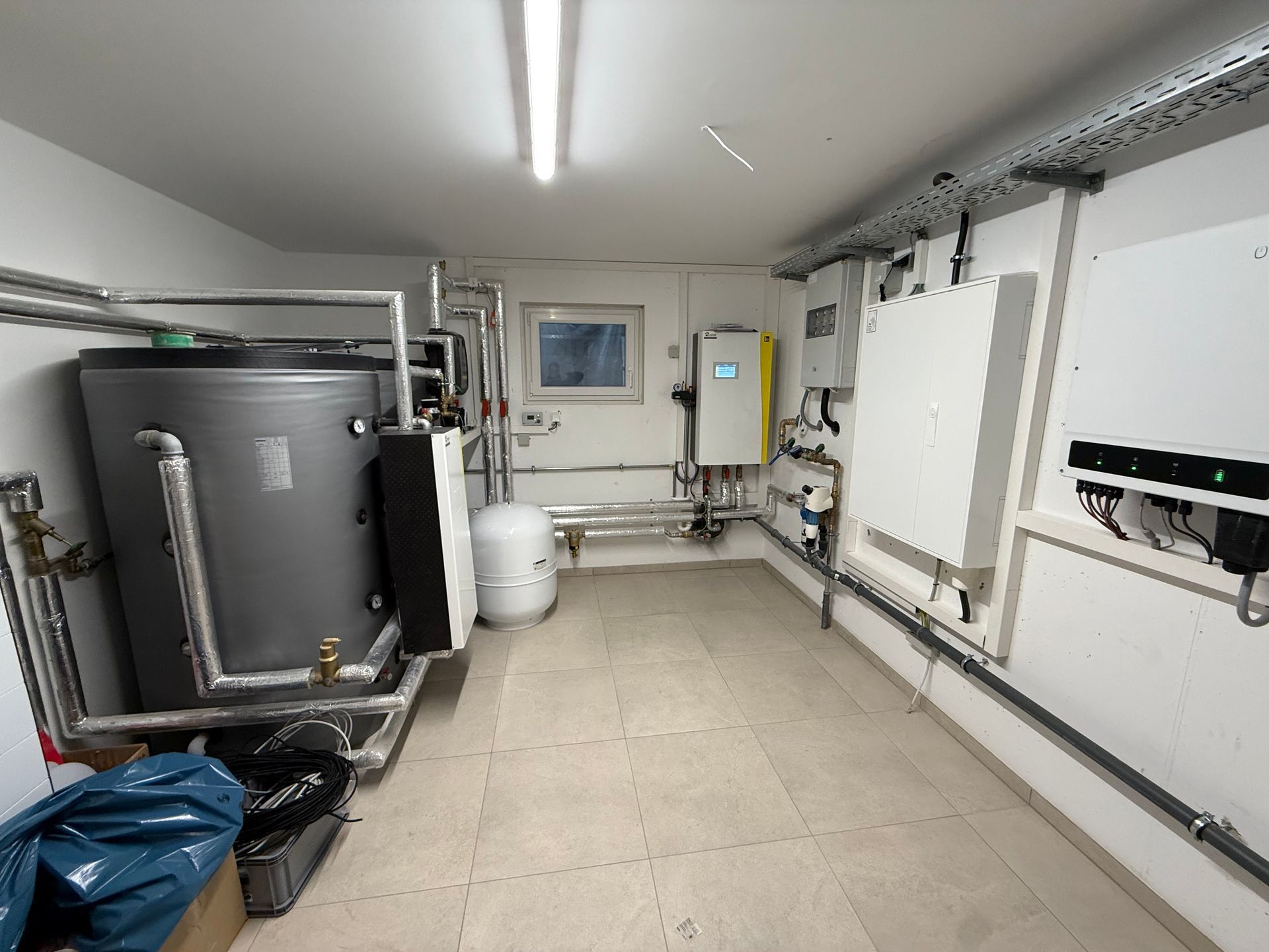 Großer Technikraum mit Warmwasserspeicher, Steuerungseinheiten und umfangreicher Heizungsinstallation.