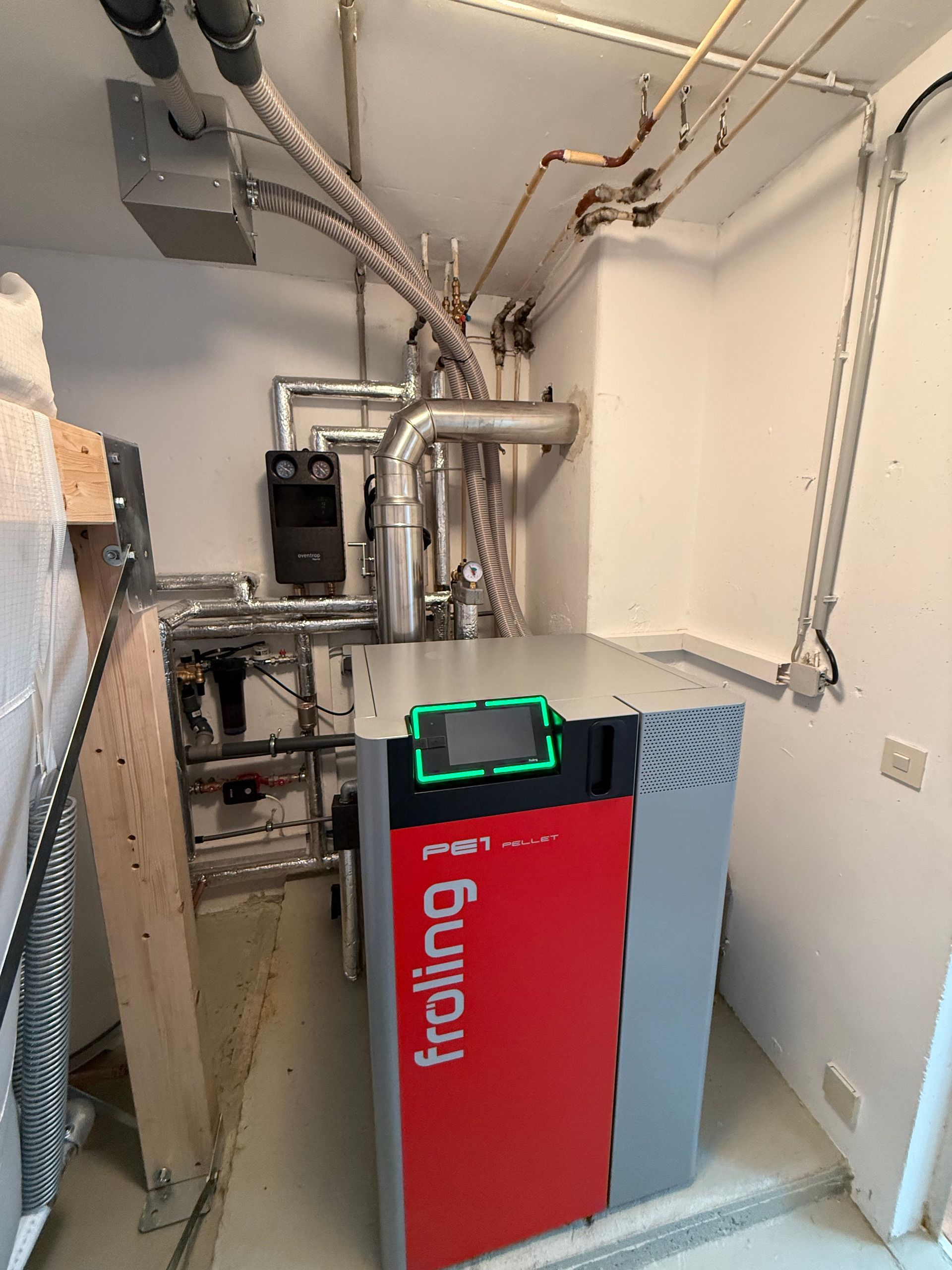Moderne Pelletheizung (Froling PE1) im Technikraum mit Rohrsystem und digitalem Display.