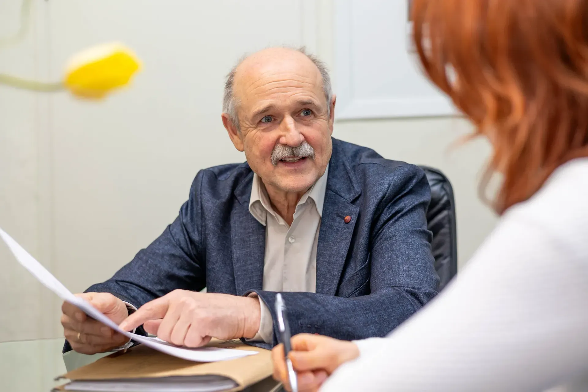 Ein Mann sitzt an einem Tisch und unterhält sich mit einer Frau, während er ein Blatt Papier in der Hand hält.