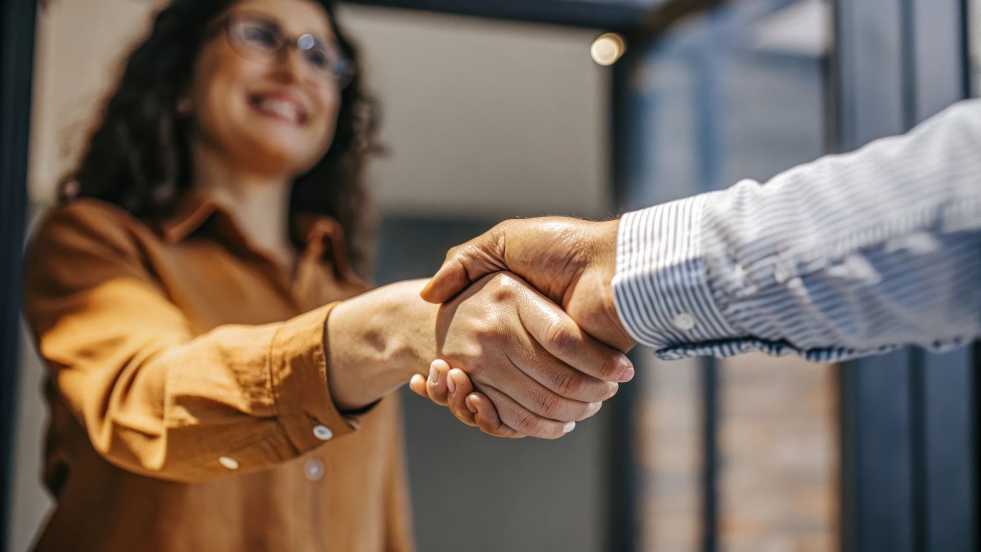 Femme portant des lunettes et une chemise jaune serrant la main d'un homme en chemise rayée