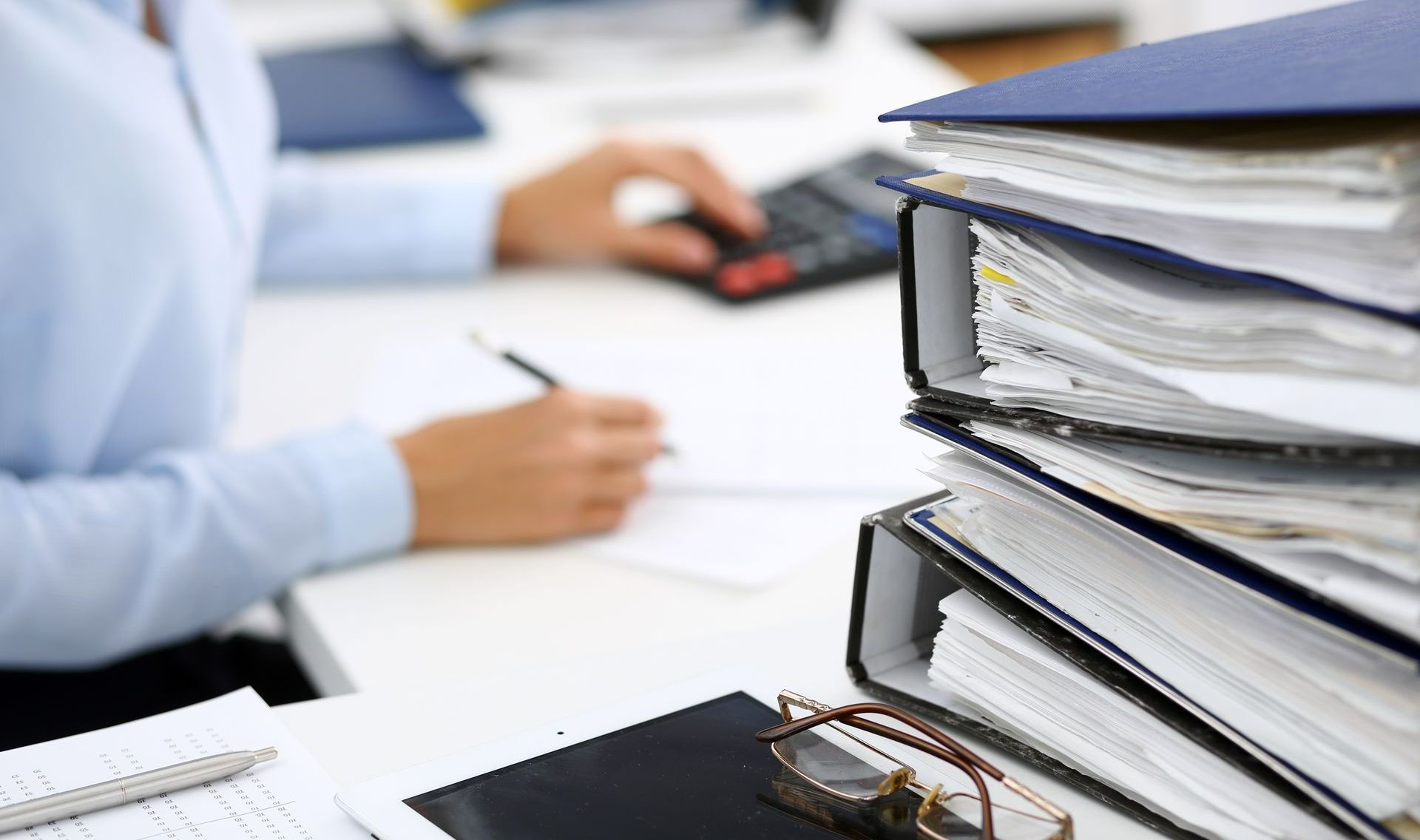 Silhouette de femme pianotant sur une calculatrice et pile de classeurs