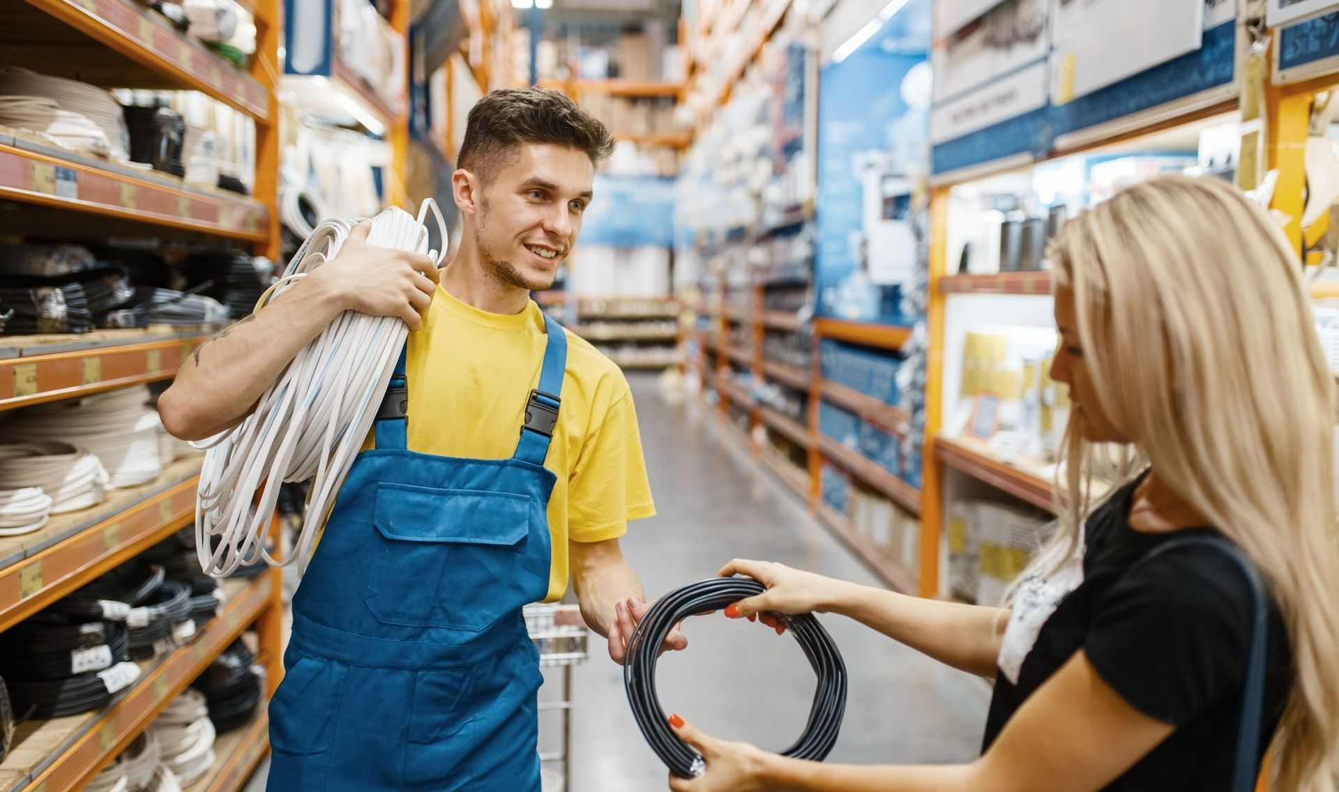 Jeune homme en t-shirt jaune portant un rouleau de câbles discutant avec une femme lui présentant un câble