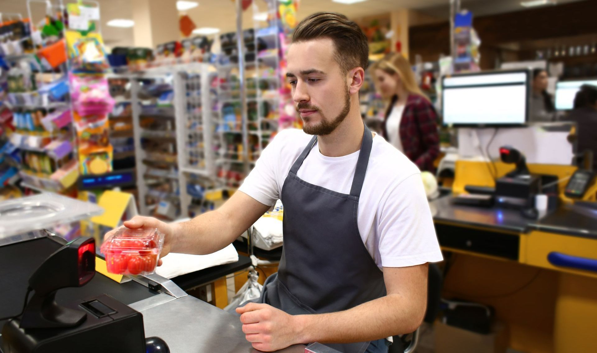 Caissier en tablier dans un supermarché scannant une boîte de tomates