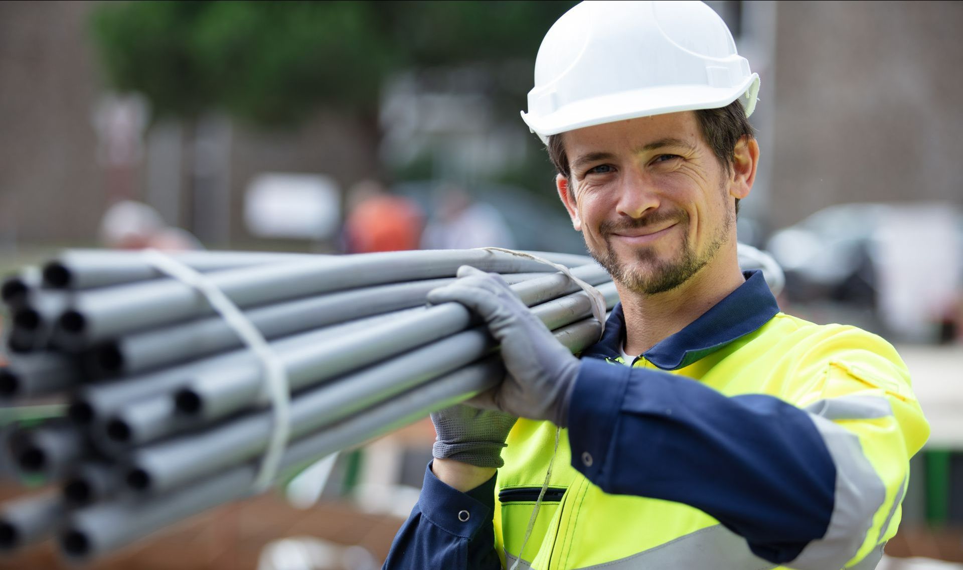 Homme portant un casque blanc, un gilet jaune et des tuyaux sur l'épaule