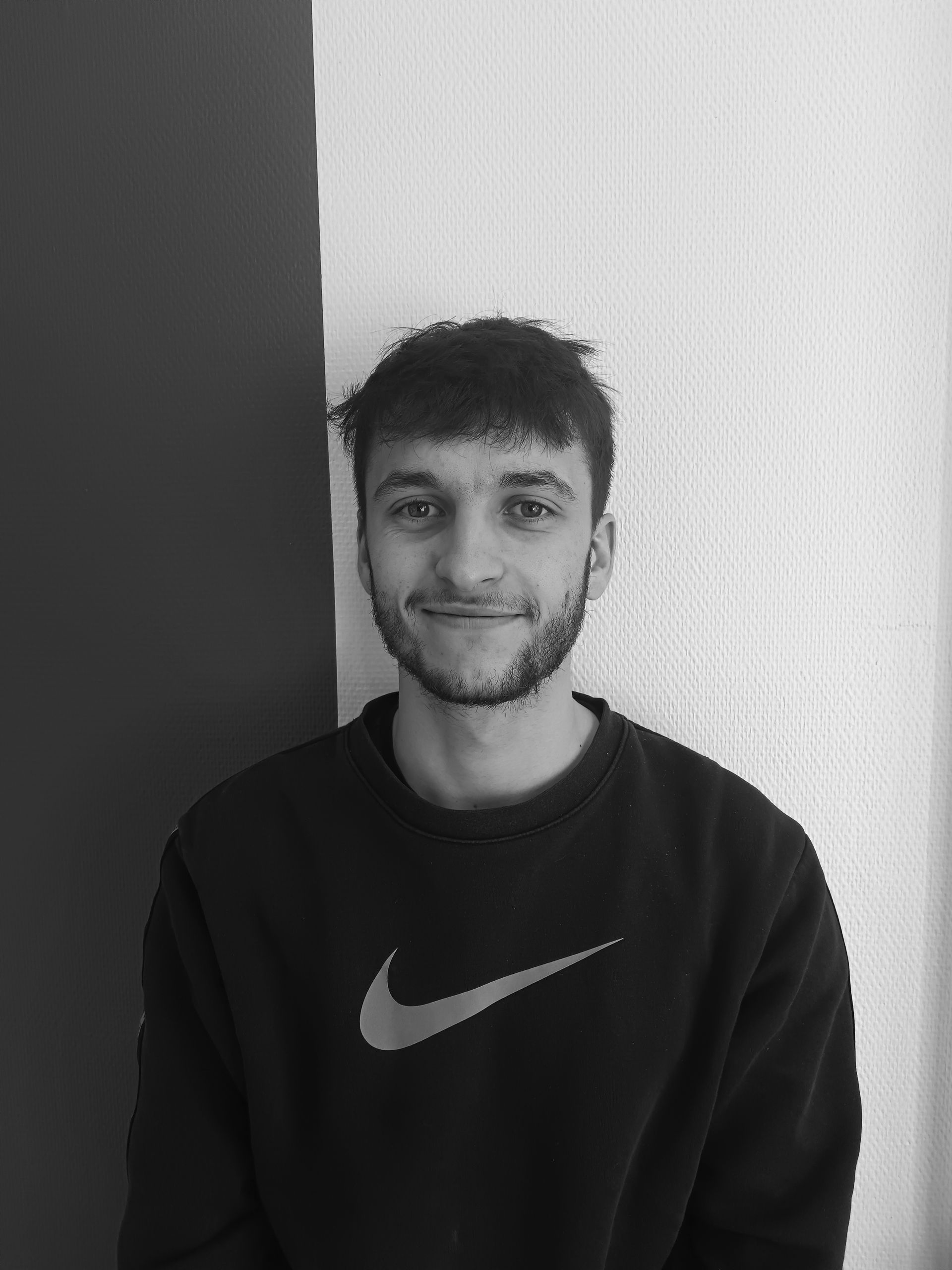 Un homme portant un sweat-shirt Nike souriant devant un fond neutre.