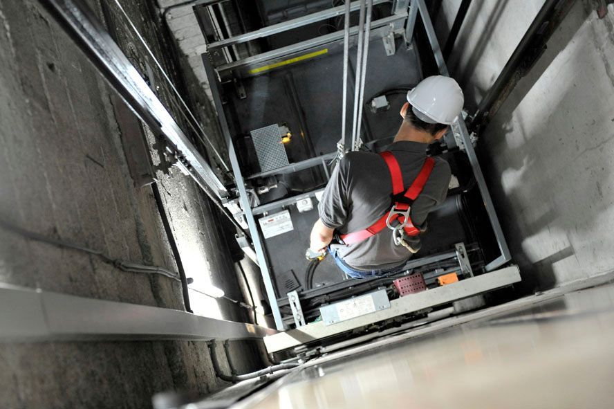 Technicien d'ascenseur harnaché, travaillant à l'intérieur d'une cage d'ascenseur.