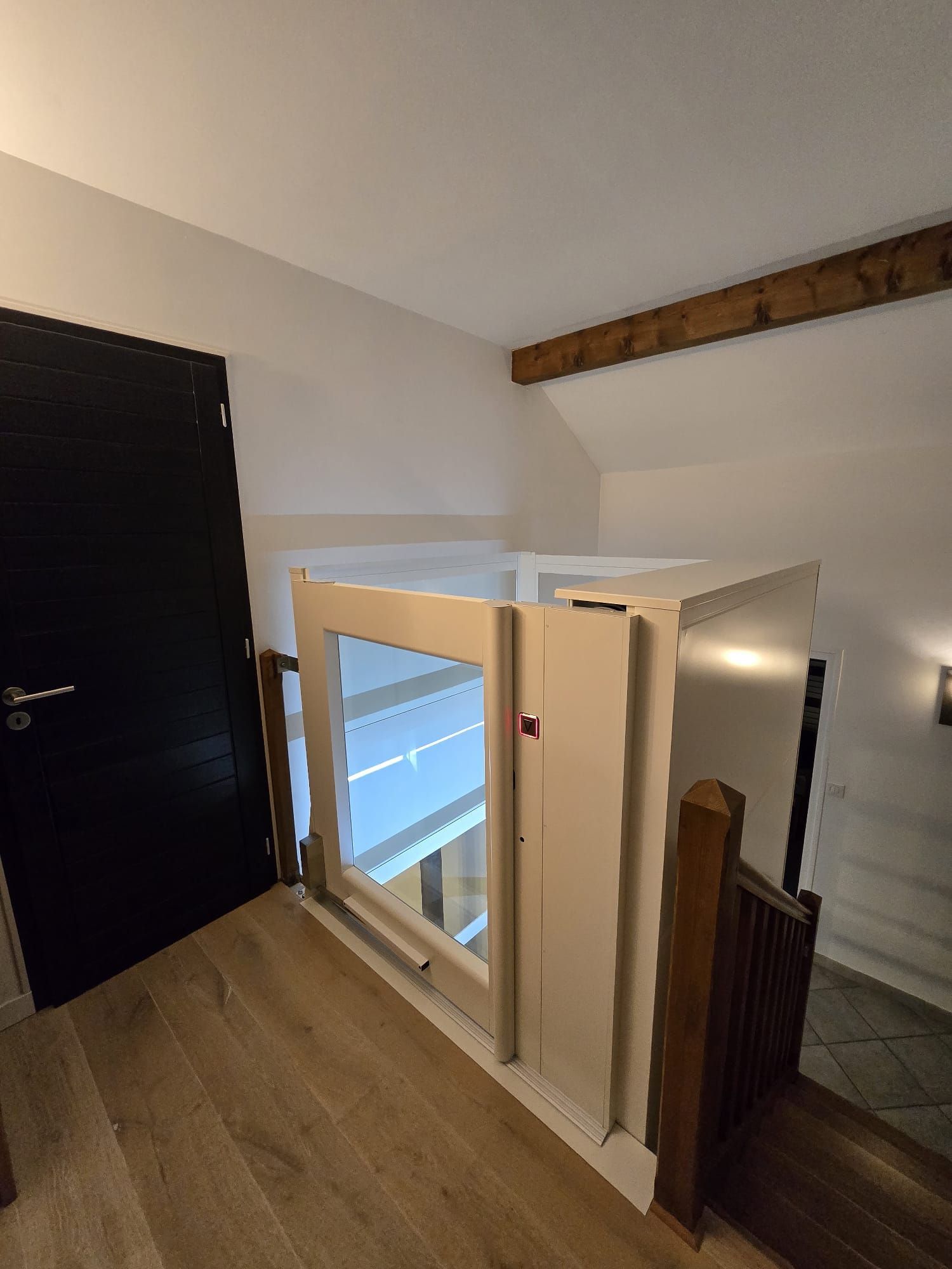 Un monte-escalier sur un palier à côté d'une porte, une rampe en bois et des poutres.