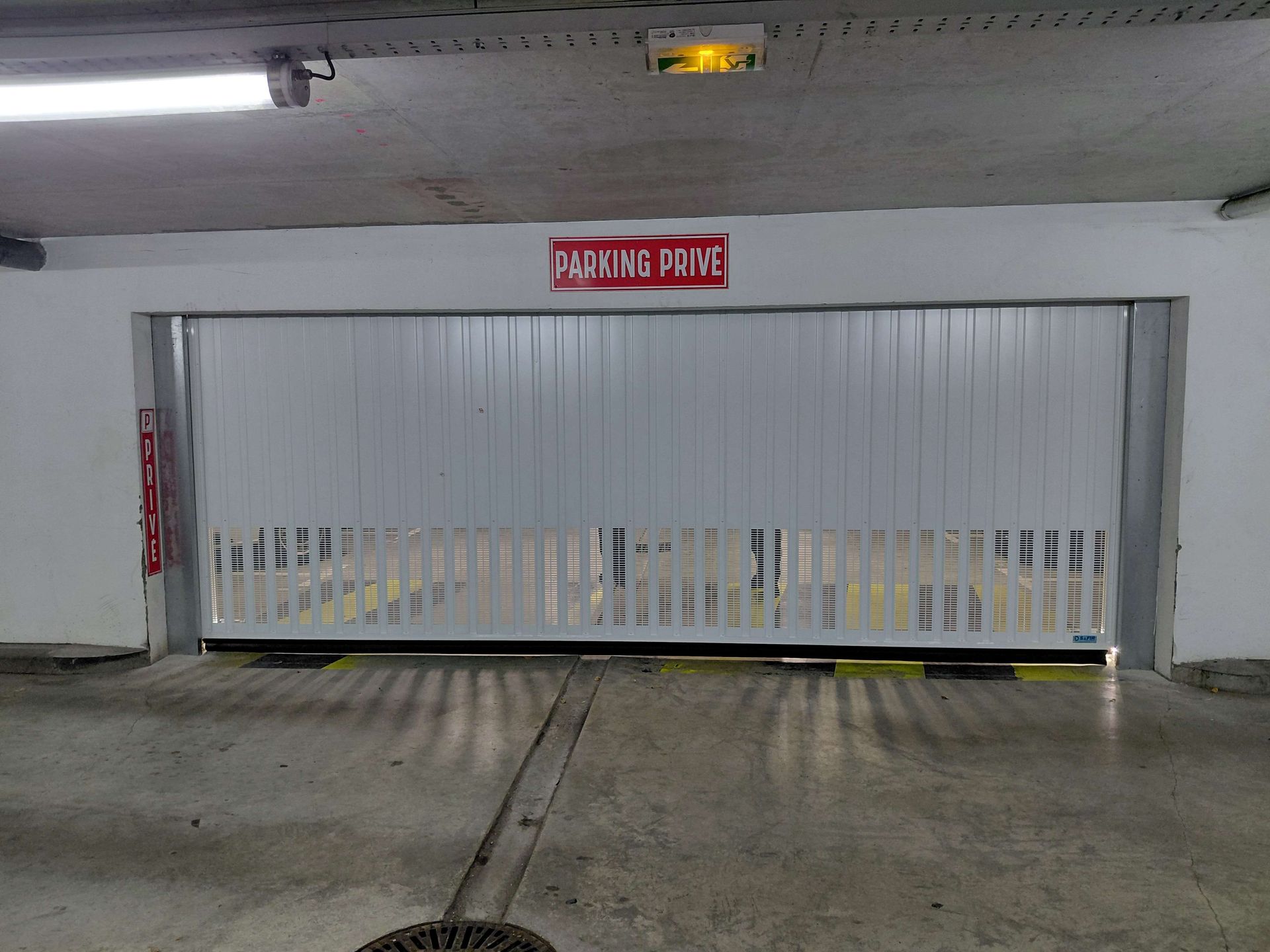Portail métallique blanc à l'entrée d'un parking souterrain, avec un panneau rouge au-dessus indiquant « STATIONNEMENT INTERDIT AUX FFAS ».