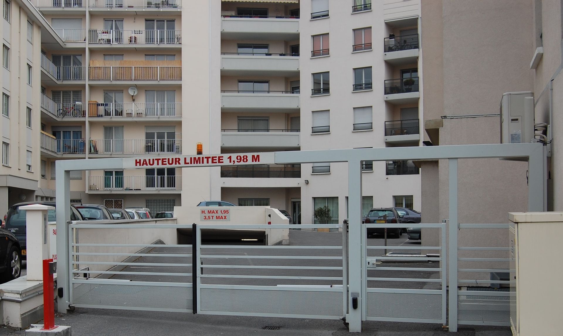 Portail d'entrée d'un parking souterrain limité à 1,90 m de hauteur. Bâtiments en arrière-plan.