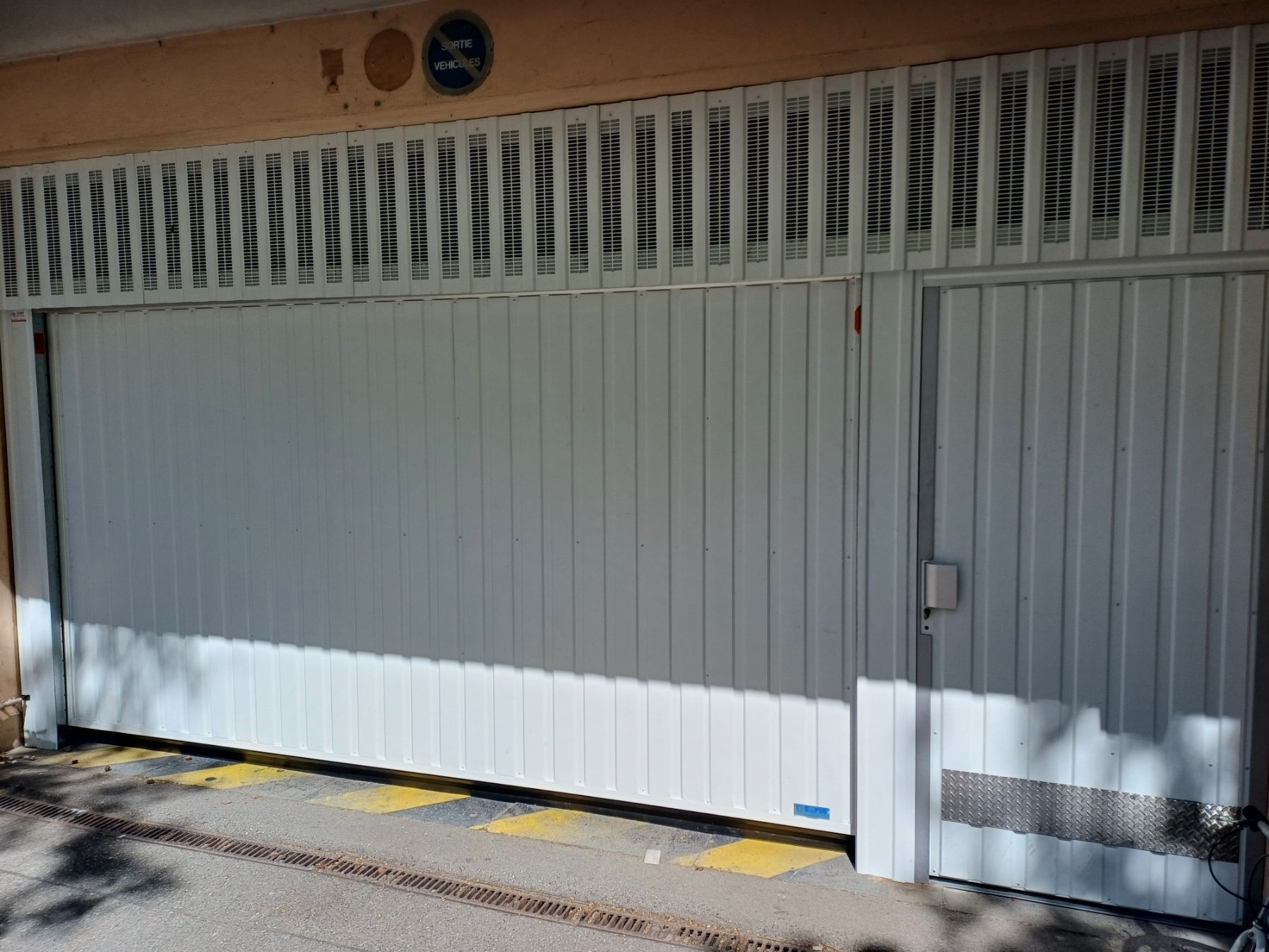 Portail et porte en métal blanc, entrée du bâtiment. Marquages ​​de signalisation jaunes et noirs au sol.