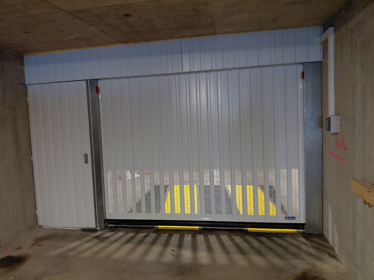 Portail coulissant industriel blanc partiellement ouvert dans un tunnel en béton.