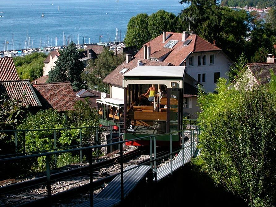 La cabine du funiculaire descend, offrant une vue imprenable sur les toits et un lac avec des bateaux.