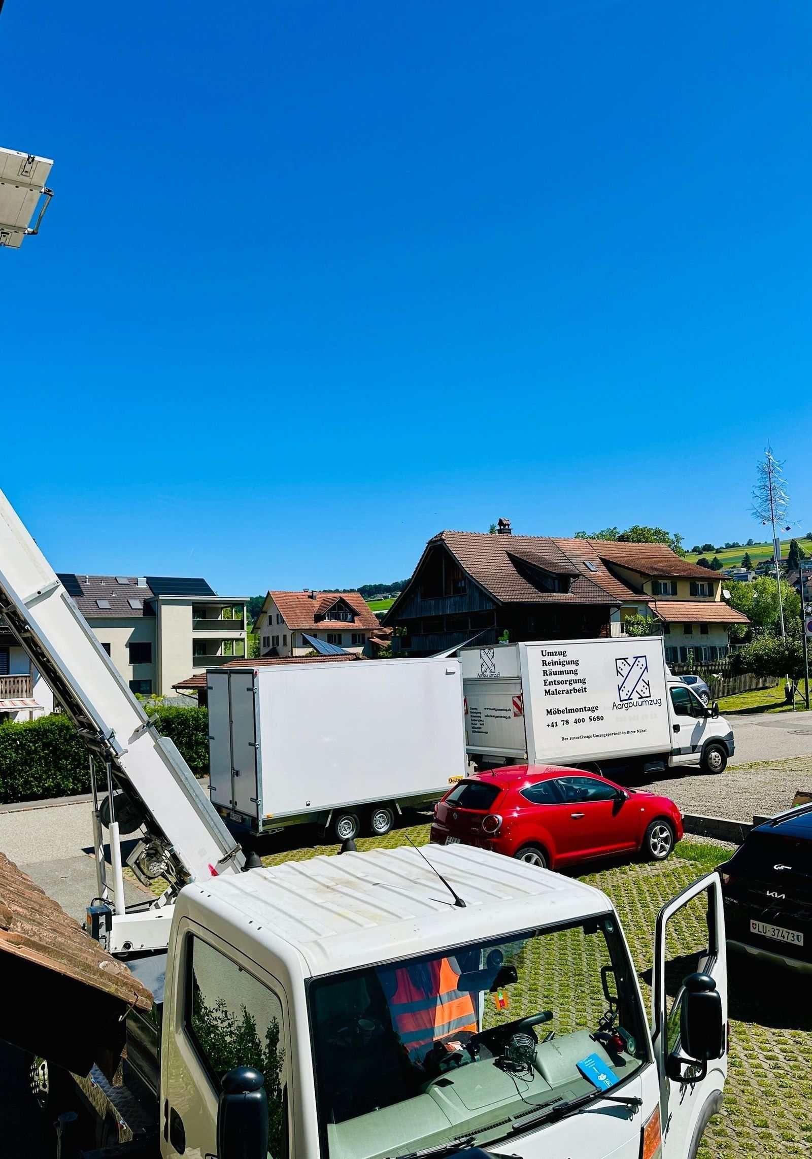 Vorstadtstrasse mit geparkten Lastwagen, einem roten Auto, Häusern und einem strahlend blauen Himmel