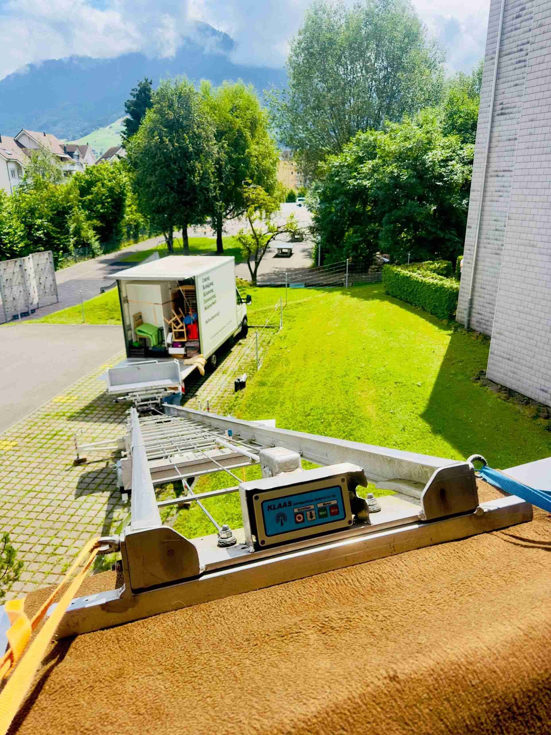 Sonniger Hof mit einem weissen Lieferwagen neben einem grünen Rasen und Steinstufen neben einem Gebäude