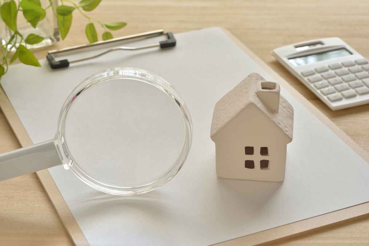 Loupe avec une maquette de maison sur un bloc-notes et une calculatrice sur la droite