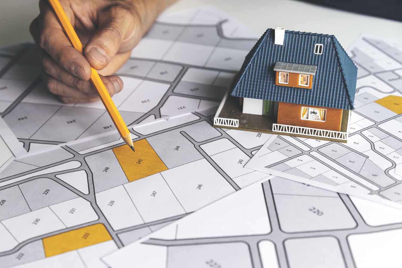 Un homme pointe un crayon sur un plan urbain sur lequel est posée une maquette de maison