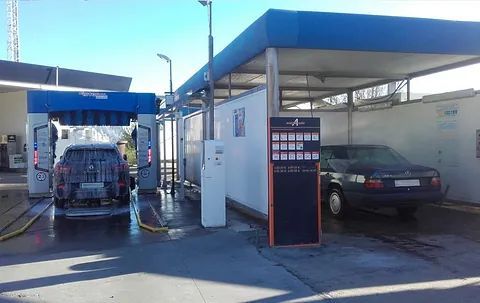 Una instalación de lavado de automóviles con un automóvil dentro del área de lavado y otro automóvil estacionado en un área de lavado.