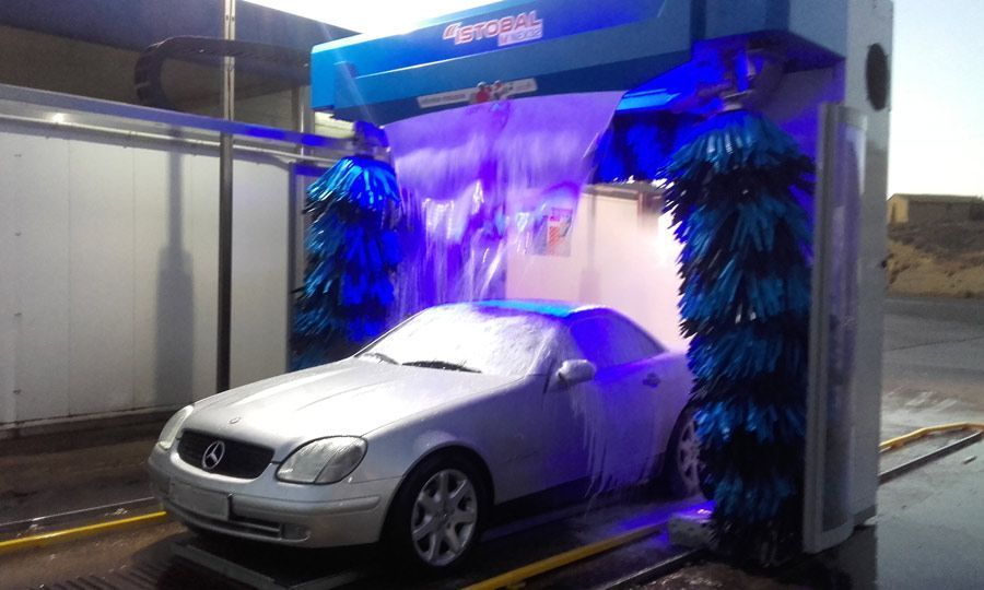 Un coche plateado se lava en un lavadero de coches, rodeado de cepillos azules y agua.