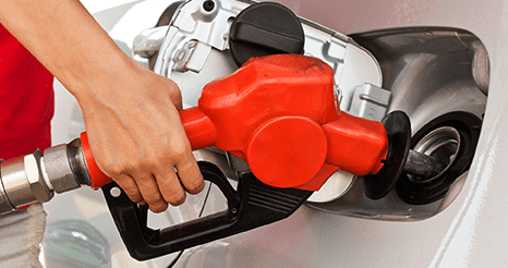 Una persona cargando combustible en un automóvil con un surtidor de gasolina rojo en una gasolinera.