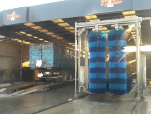 Lavado de camión en un lavadero. Cepillos giratorios azules y blancos frotan el vehículo.