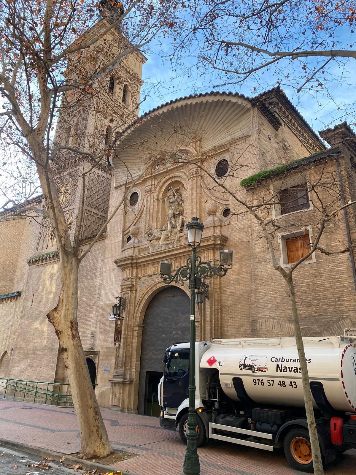 Un árbol de Navidad iluminado junto a un camión blanco con tanque en una calle adoquinada por la noche.