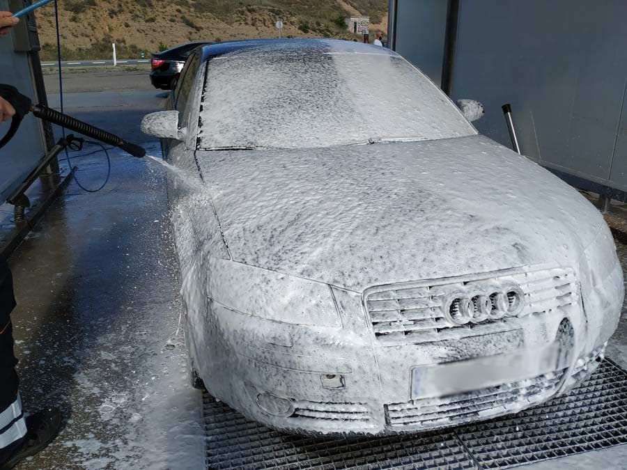 Un coche cubierto de espuma blanca siendo rociado con agua en un lavadero de coches.