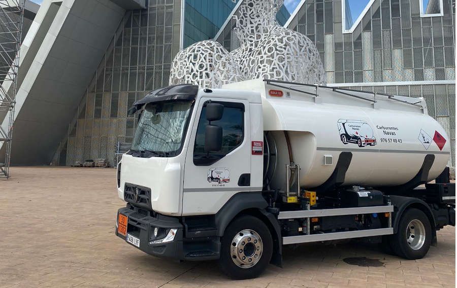 Camión cisterna de combustible blanco estacionado frente a un edificio moderno con esculturas esféricas.