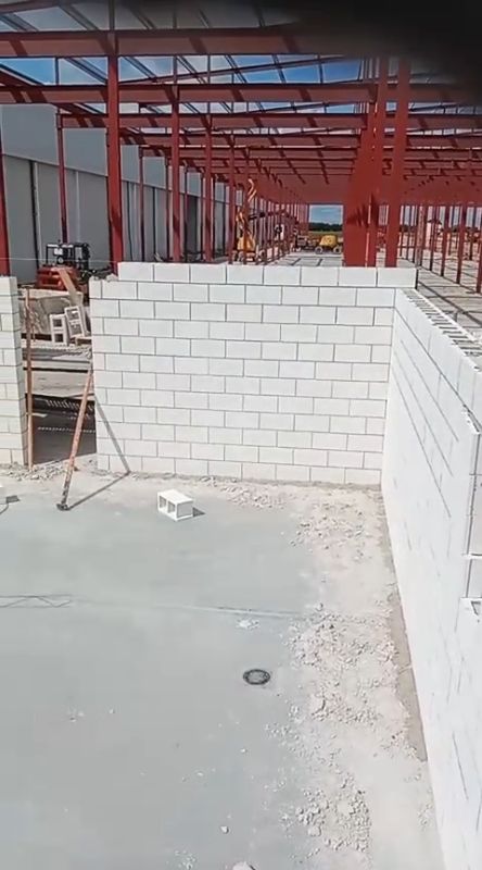 Obra en construcción con paredes de bloques blancos, estructura de acero rojo y suelo de hormigón.