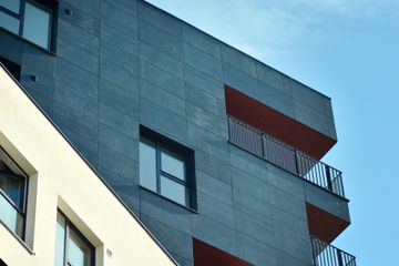 Edificio de apartamentos moderno con fachada gris oscuro, balcones rojos y cielo azul.