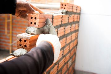 Manos colocando ladrillos con mortero en una pared en una obra de construcción.