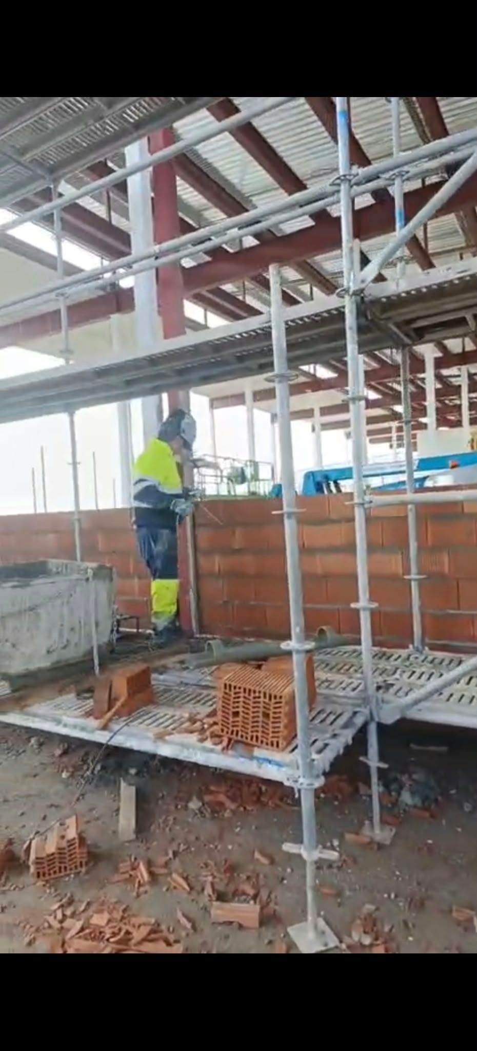 Obrero con chaleco amarillo en un andamio en una obra de construcción de ladrillos.