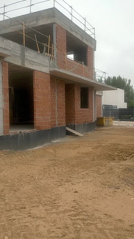 Casa de ladrillo parcialmente construida con andamios y planta superior sin terminar en un terreno arenoso.