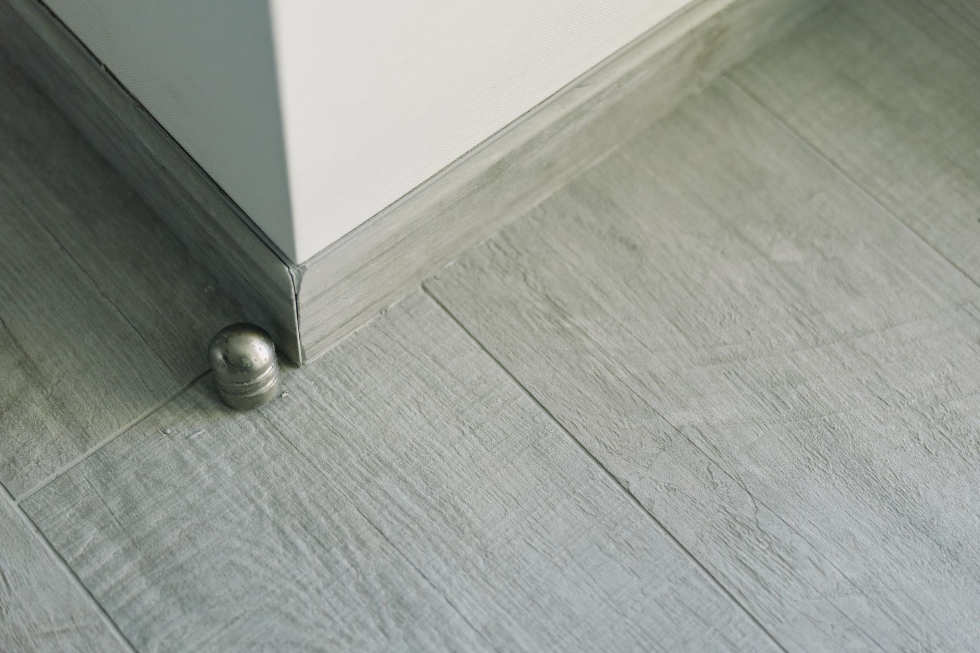 Rincón de una habitación con suelo de madera gris y una pequeña bola plateada cerca del borde de una pared.
