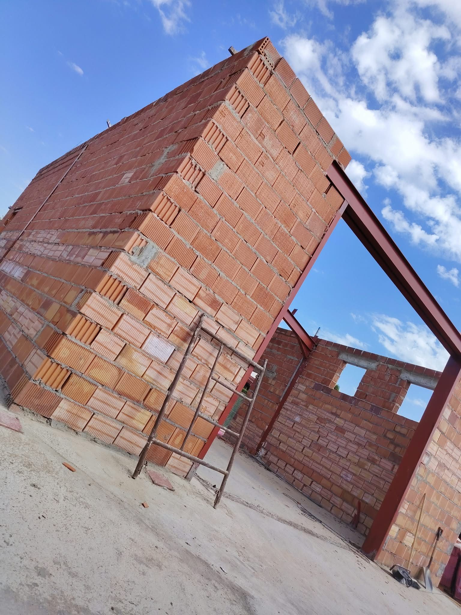Edificio de ladrillos sin terminar con una escalera apoyada contra una pared bajo un cielo azul.