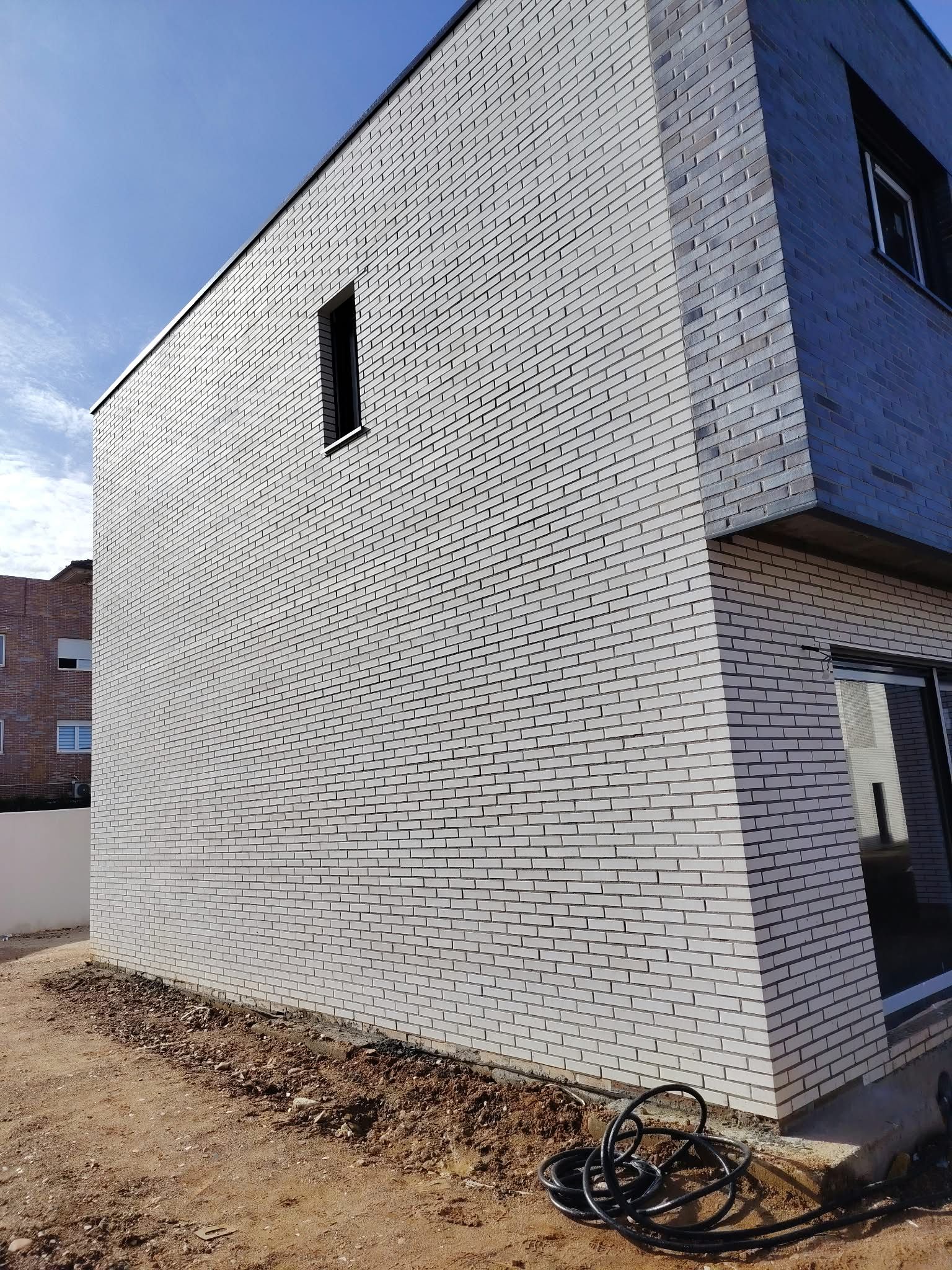 Muro blanco del edificio con un mural en espiral negro y una pequeña ventana bajo un cielo azul.