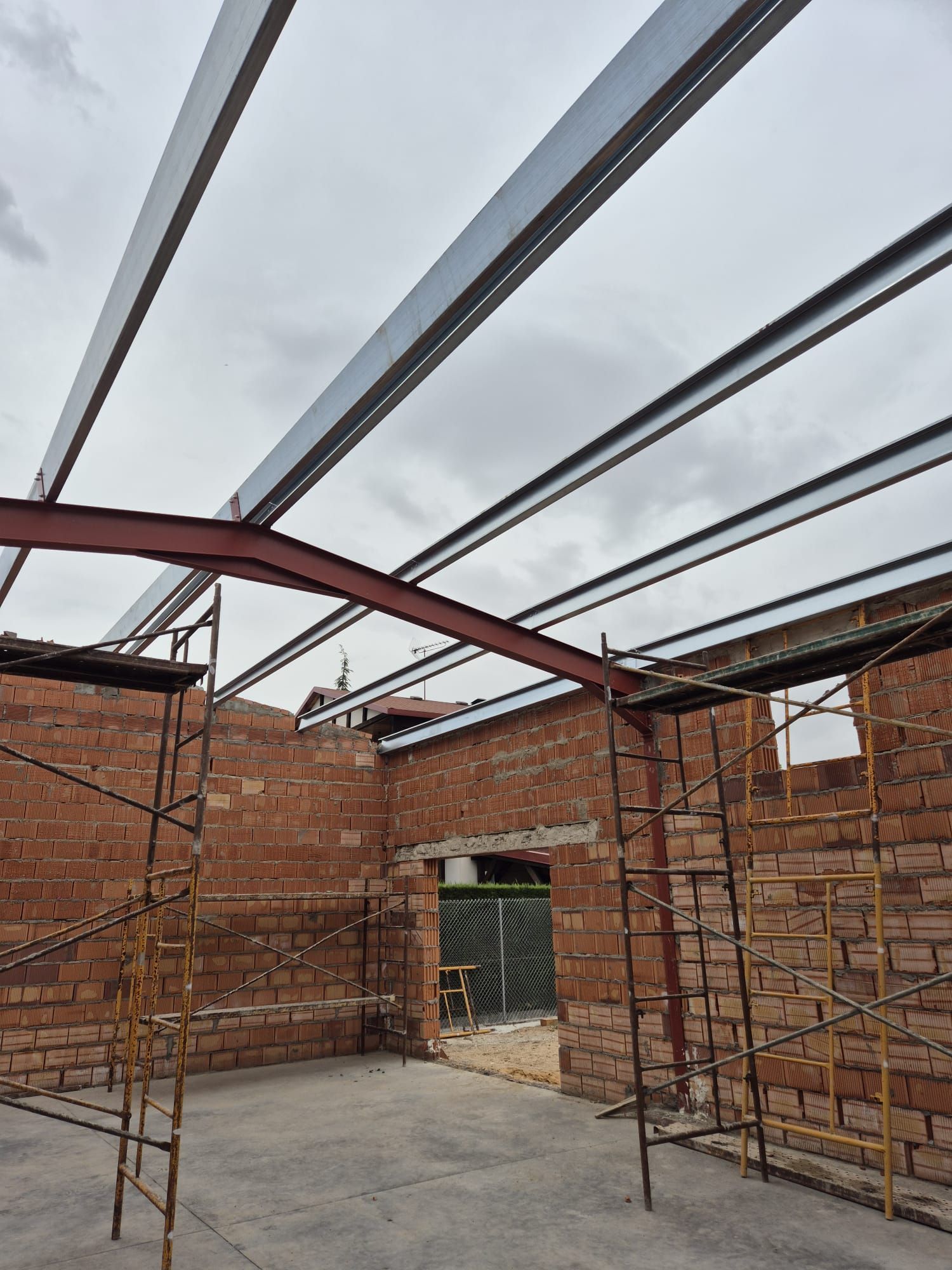 Edificio de ladrillo en construcción con vigas de acero en el techo y andamios dentro de una habitación sin terminar.
