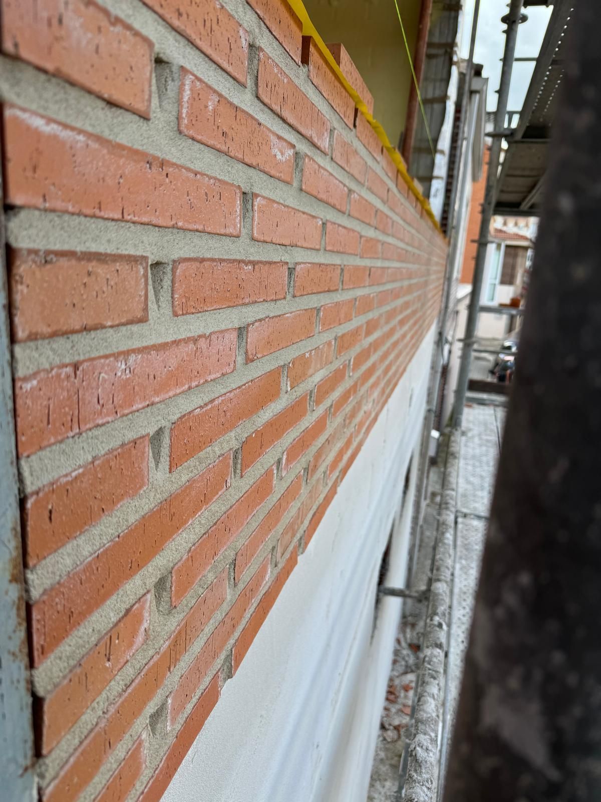 Muro de ladrillo rojo con molduras blancas en el exterior de un edificio, visto desde un andamio de construcción estrecho.