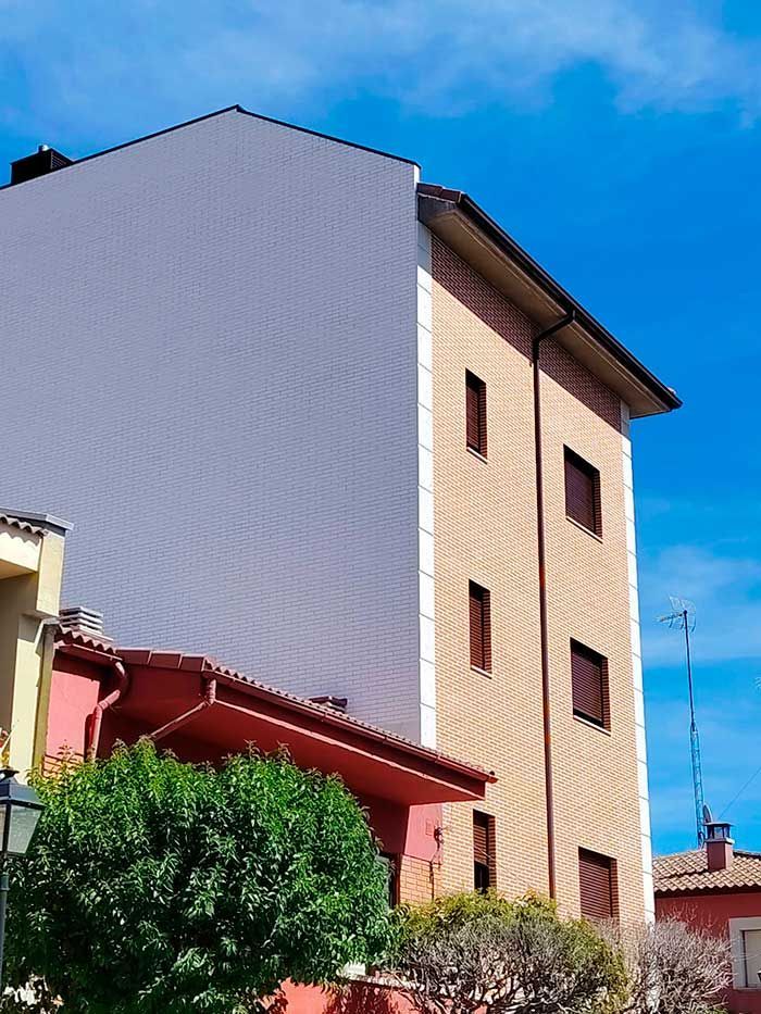 Edificio de apartamentos alto con paredes beige y blancas, toldos rojos y cielo azul en lo alto.